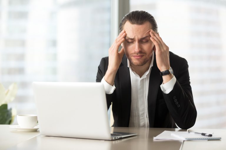 Businessman at work with his hands on his temples due to a headache from anxiety