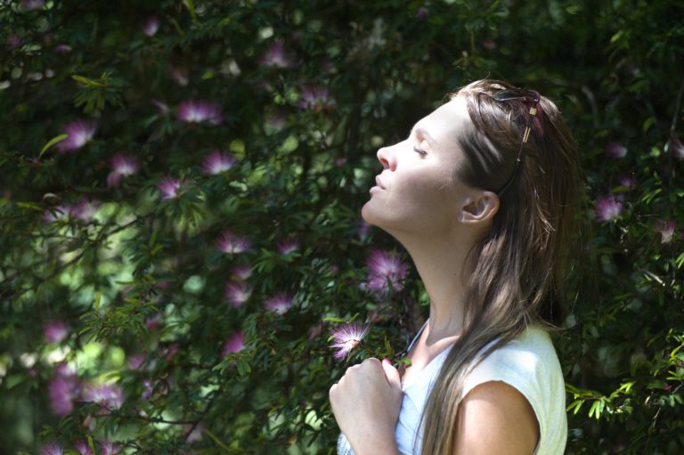 Woman taking a deep breath outside near plants and trees