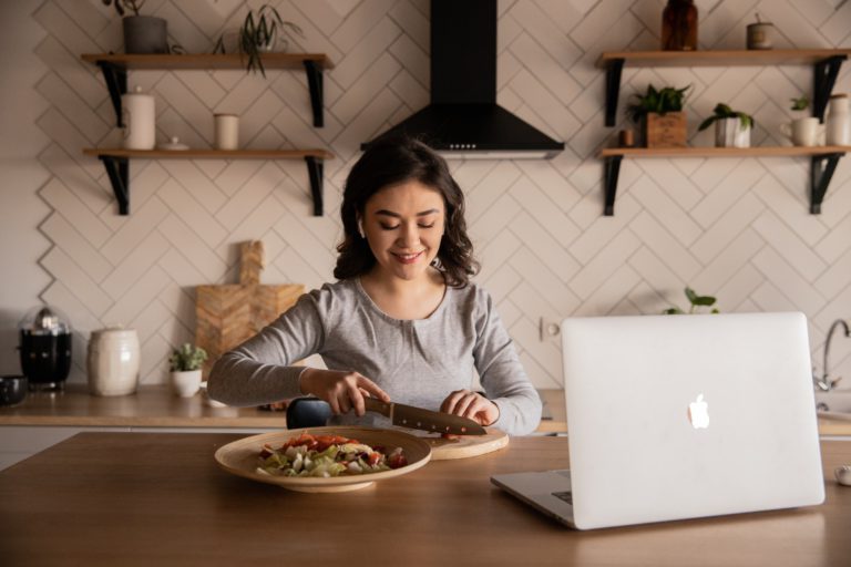 Woman cooking a meal at home in front of her laptop